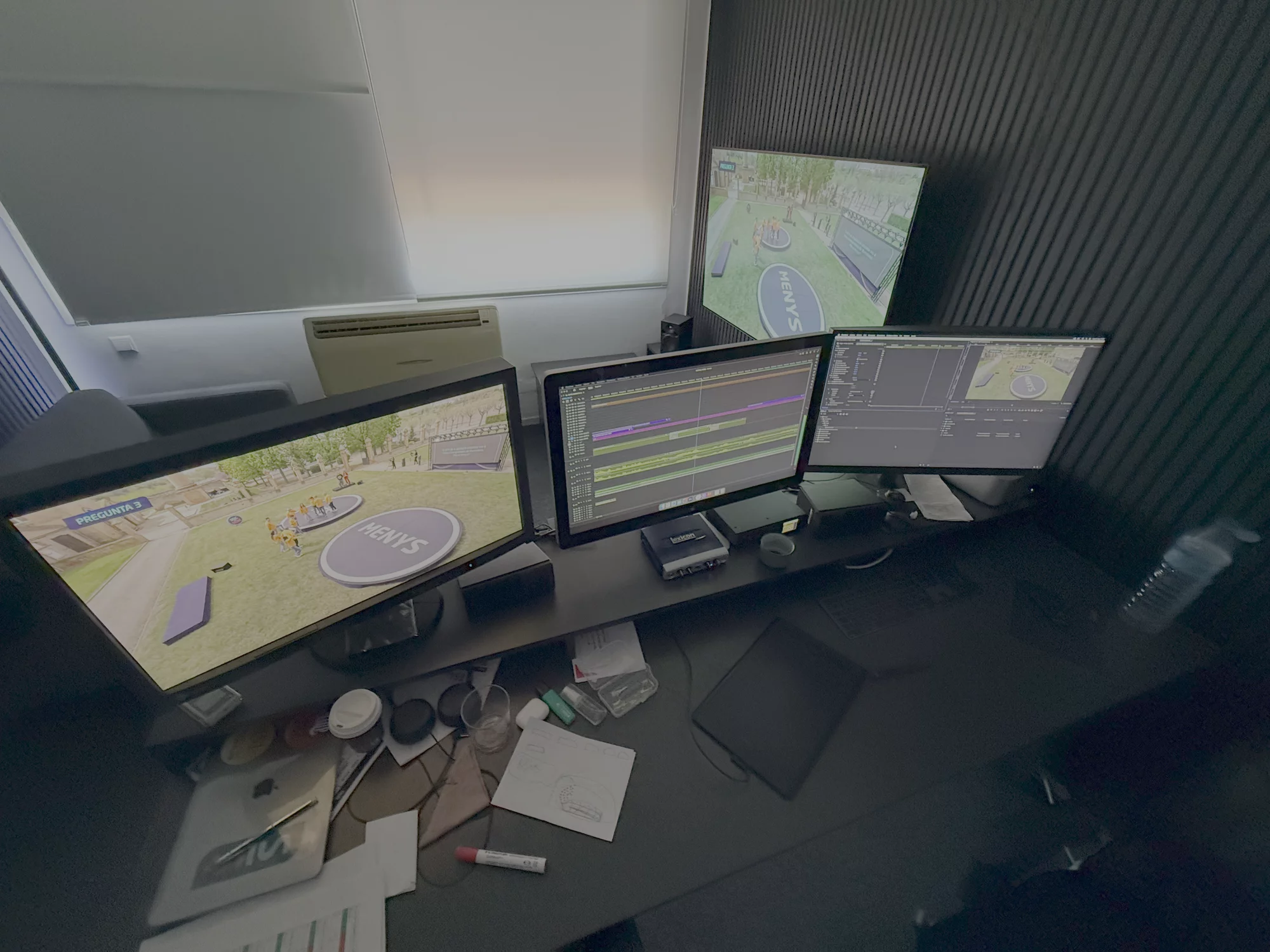 Escritorio con tres monitores exhibiendo entornos virtuales y software de edición de vídeo.