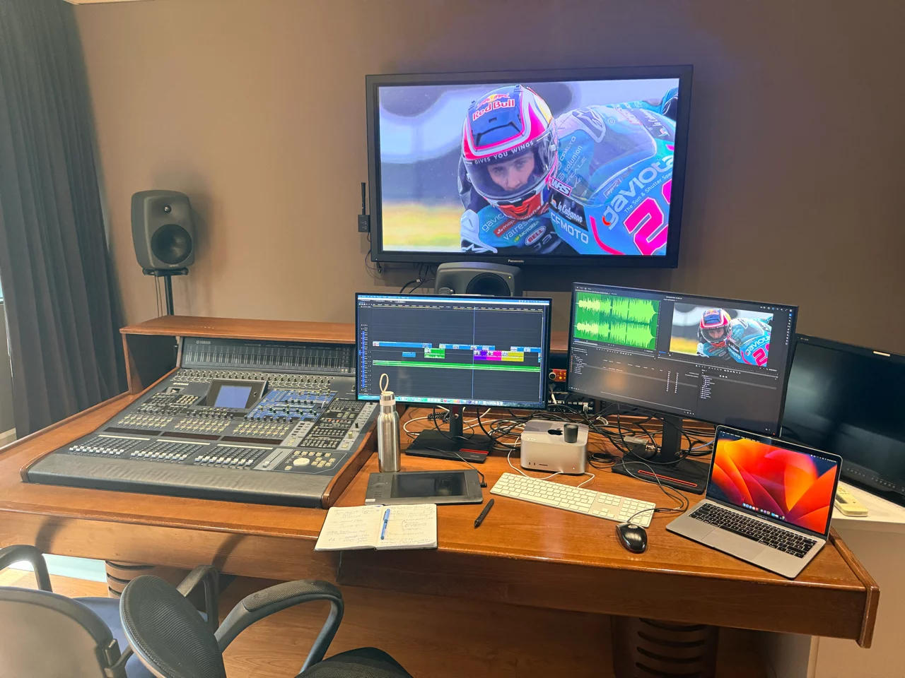 Estudio de postproducción con consola de mezcla, múltiples pantallas y vídeo de carreras.